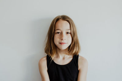 Calm adorable teenage girl with freckles in casual top standing against white background and looking at camera