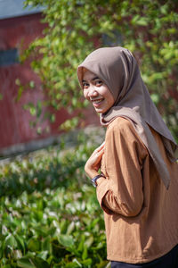 Side portrait of a beautiful woman wearing a modern hijab in a garden with left hand on her chest