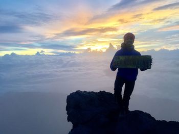 Man standing on rock against sky during sunset