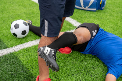 Low section of male physical therapist stretching soccer player leg on field