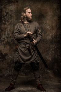 Young man with sword standing against wall