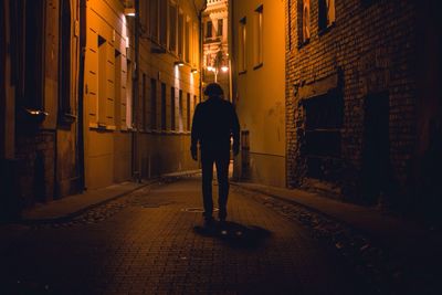 Full length rear view of silhouette man standing in illuminated alley