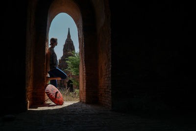 Rear view of woman with traditional paper umbrella standing in arch formed entrance of pagoda