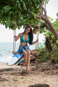 Full length portrait of young woman sitting on swing at beach