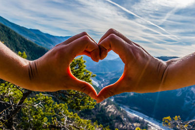 Cropped image of hands heart shape against sky