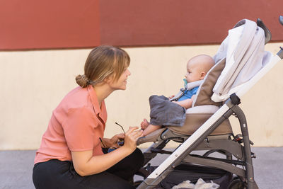 Portrait of young mother with her baby in a child carrier drinking a coffee while scrolling 