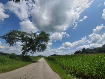 Empty road amidst field against sky