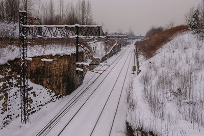 Snow covered railroad tracks by trees during winter