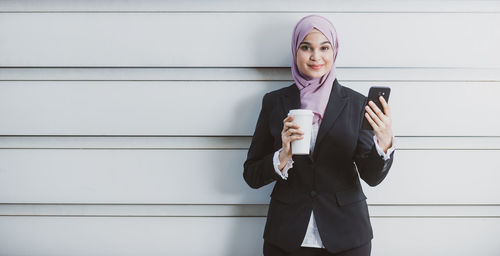 Full length of a woman holding coffee cup against wall