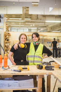 Portrait of smiling young female coworkers standing with arm around at workbench