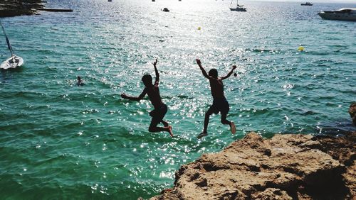High angle view of silhouette boys jumping in sea