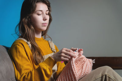 Young woman knitting sweater at home