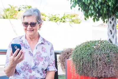 Senior woman using phone while sitting by plant