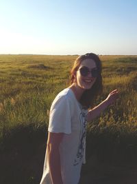 Portrait of smiling young woman standing on field against clear sky