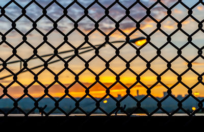 Close-up of chainlink fence against sky during sunset