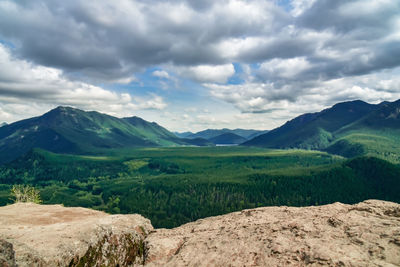 Green mountain valley from hiking ledge overlook under dramatic sky.