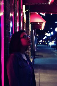 Young woman standing against illuminated wall at night