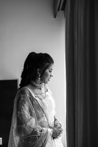 Black and white photography of woman looking thru the window  while standing at home