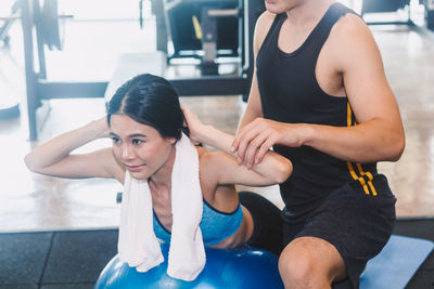 Midsection of instructor assisting woman in exercising at gym