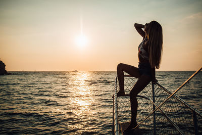 Man sitting on sea against sky during sunset