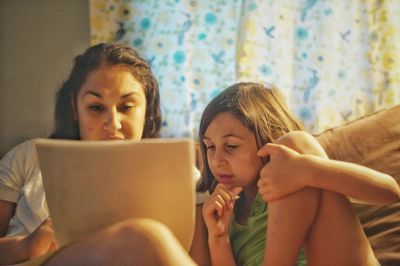 Mother teaching daughter while sitting on sofa at home