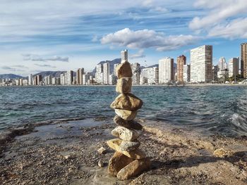 Rocks in balance by sea against sky in city