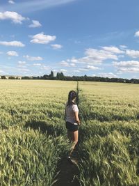 Rear view of woman standing in field against sky