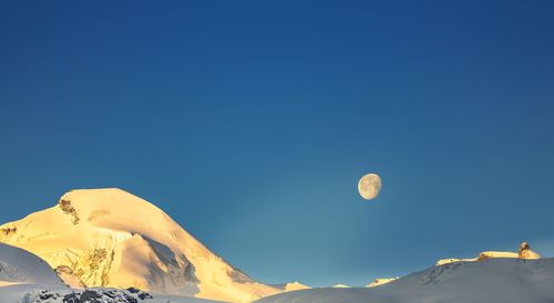 Low angle view of snowcapped mountains against clear blue sky