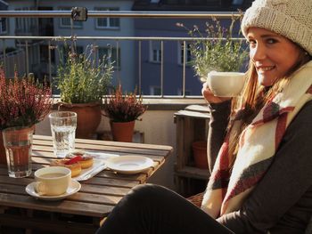 Side view of woman drinking drink while resting on balcony in city