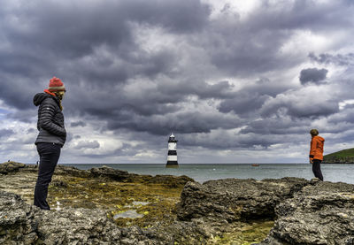People standing on rock by sea against sky