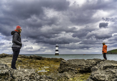 People standing on rock by sea against sky