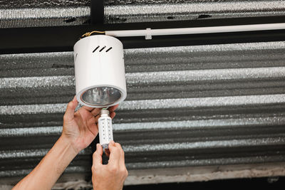 Close up human hand is installing an led light bulb in a circular ceiling lamp.