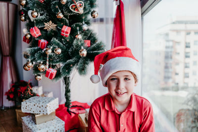 Beautiful kid boy at home with presents by the christmas tree