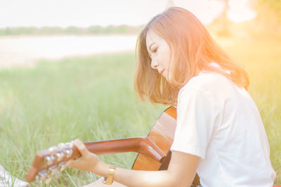 Young woman playing guitar on grassy field at park