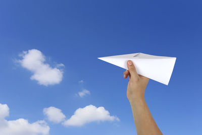 Cropped hand holding paper airplane against blue sky