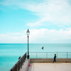 Side view of boy walking by railing against sea and sky