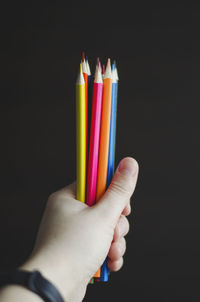 Close-up of hand holding colored pencils against black background