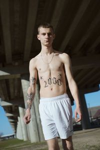 Portrait of shirtless young man with tattoo standing outdoors