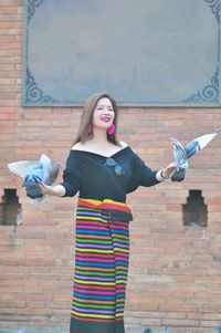 Portrait of woman with birds standing against brick wall