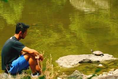 Side view of man sitting on rock at lakeshore