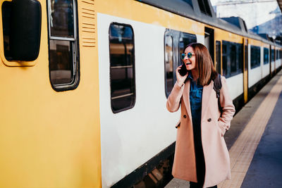 Woman with phone standing by train on railroad station platform