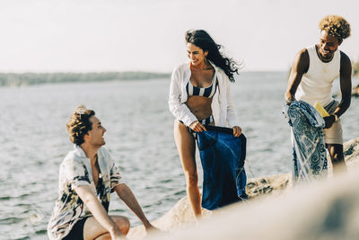 Happy male and female friends talking with each other while packing stuff after swimming at lake