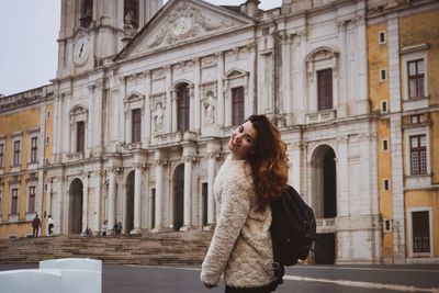 Portrait of young woman standing against built structure in city