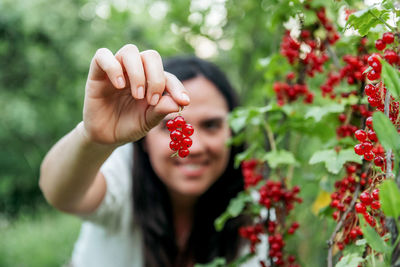 Selective focus photo of young woman holding cluster of redcurrant outdoor in garden