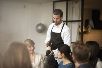 Man wearing apron showing wine bottle to business people during winetasting