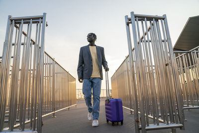 Smiling businessman with suitcase walking admist railings