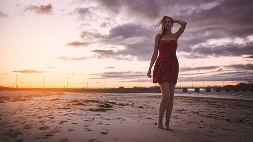 Woman looking away while standing on beach against sky during sunset