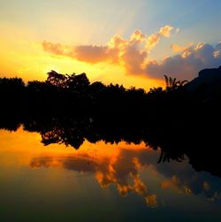 Silhouette trees by lake against sky during sunset