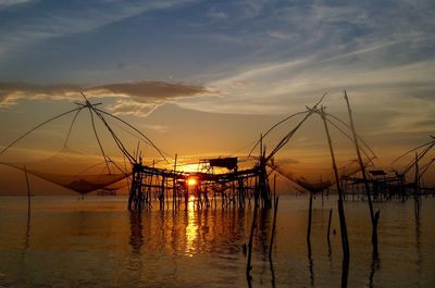 Silhouette fishing net by sea against sky during sunset