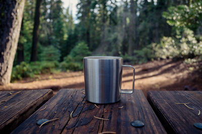 Coffee mug on table against trees in forest